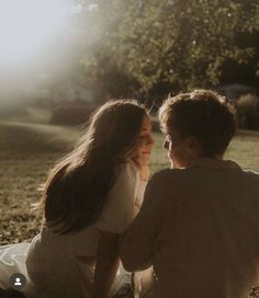 a woman sitting next to a man on top of a grass covered field