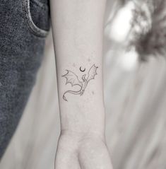 a small tattoo on the wrist of a woman with a dragon and moon behind it