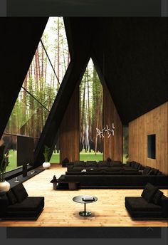 a living room filled with black couches next to wooden walls and trees in the background