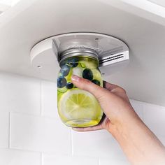 a person holding a mason jar filled with blueberries, lemons and cucumbers