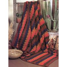 a crocheted blanket sitting on top of a wooden floor next to cacti