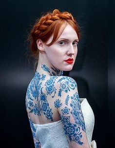 a woman with red hair and blue tattoos on her body is looking at the camera