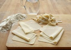 some uncooked pasta sitting on top of a wooden cutting board next to flour