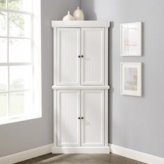 a white cabinet sitting in the corner of a room next to a wall with pictures on it