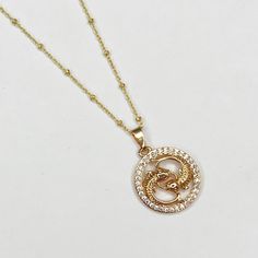 a gold plated necklace with a snake in the center on a white table top