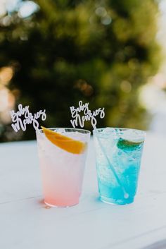 two drinks sitting on top of a white table next to each other in front of trees