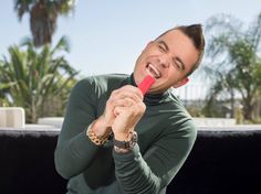 a man is brushing his teeth with a red toothbrush in front of palm trees