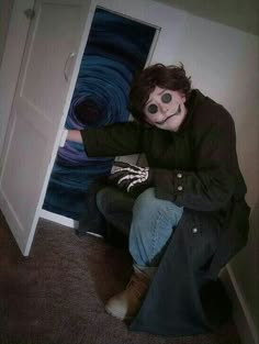 a man sitting on the floor in front of an open door with his face painted like a skeleton