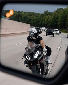 a rear view mirror shows a man on a motorcycle driving down the road in traffic