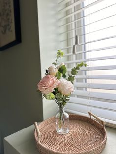 a vase with flowers sitting on top of a wicker tray next to a window