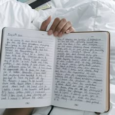 a person laying in bed holding an open book with writing on the pages and hand