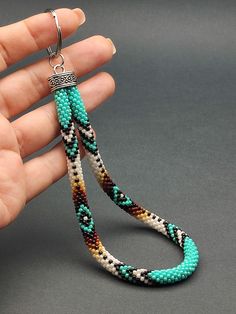 a hand holding a pair of multicolored beaded earrings on a gray background