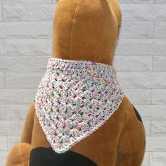 a teddy bear with a crocheted bandana on it's neck sitting in front of a brick wall