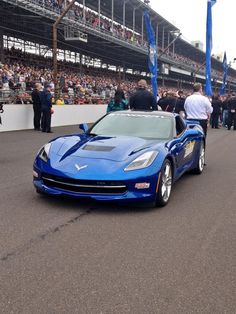 a blue sports car driving down a race track in front of a large group of people