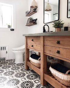 a white toilet sitting next to a wooden cabinet in a bathroom with black and white floor tiles