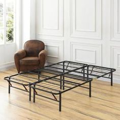 a bed frame sitting on top of a hard wood floor next to a brown chair