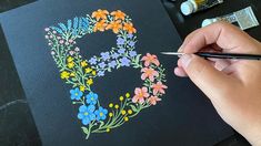 a person is drawing flowers on a piece of black paper with colored pencils and markers