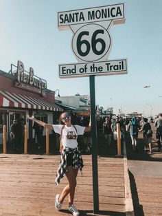 a woman standing next to a sign for santa monica 66 and end of the trail