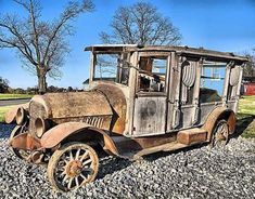 an old rusty car sitting on the side of a road next to some trees and rocks