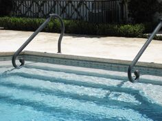 an empty swimming pool with two metal handrails in the foreground and a house in the background