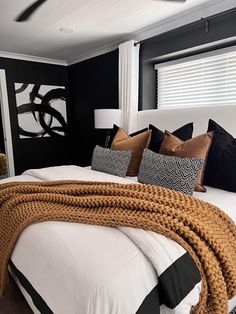 a bedroom with black walls and white bedding, brown throw pillows and blankets on the headboard