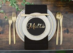 a place setting with black and white plates, gold cutlery and napkins on a wooden table