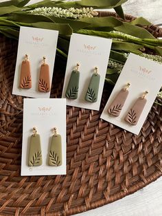 four earrings with leaves on them sitting in a basket next to some flowers and cards