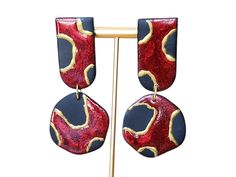 Elevate your style with these bold and sophisticated earrings! Featuring a striking red  and black pattern with gorgeous gold accents, these polymer clay dangles bring a touch of luxe to any outfit. Inspired by organic shapes and artistic flair, these statement earrings are both elegant and modern--perfect for those who want to stand out. Each pair is handcrafted with care, giving every earring a one-of-a-kind charm that reflects the beauty of imperfections. Whether you're dressing up for a special occasion or adding a pop of style to your everyday look, these earrings are sure to turn heads. Handmade with polymer clay Red and black design with hand-painted gold accents Lightweight and comfortable for all-day wear Hypoallergenic earring hooks Note: Due to the handmade nature of these earri Red Hand Painted Polymer Clay Earrings, Hand Painted Red Polymer Clay Earrings, Bold Polymer Clay Earrings For Gift, Bold Polymer Clay Earrings As Gift, Red Drop Earrings In Polymer Clay, Hand Painted Red Elegant Earrings, Elegant Hand Painted Red Earrings, Elegant Red Polymer Clay Earrings, Red Polymer Clay Earrings