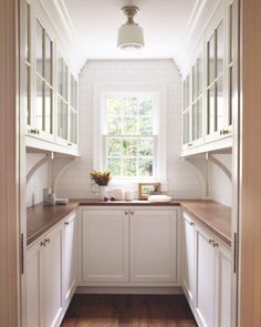 a narrow kitchen with white cabinets and wood flooring, along with a window above the sink