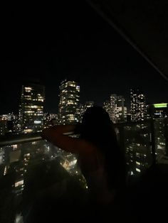 a woman standing on top of a roof at night looking out over the city skyline