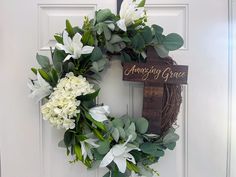 a wreath with white flowers and greenery is hanging on the front door to welcome guests