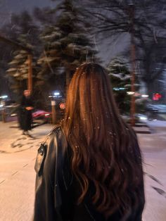 a woman walking down the street at night with snow falling all around her and trees in the background