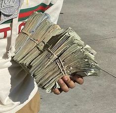 a man holding a bundle of money in his hand and wearing a white hoodie