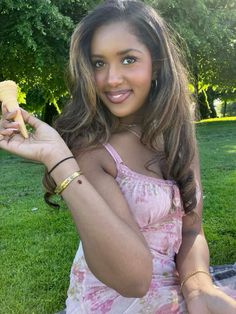 a woman sitting on the grass holding a piece of food in one hand and smiling at the camera