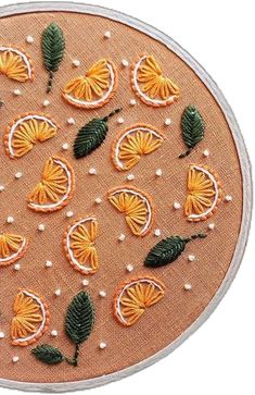 an embroidery project with oranges and green leaves on a piece of fabric, which has beading around the edges