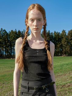 a woman with long red hair and braids standing in a field wearing a black dress