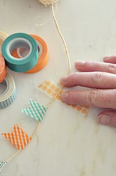 someone's hand is holding some tape and scissors on a table with other crafting supplies