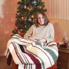 a woman sitting in a chair under a christmas tree with a blanket on her lap