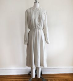 "Long-sleeved, ivory dress with pintucks and embroidered lace collar, from the 1980s. Bust measures 19\" (48.5 cm) flat across and waist measures 12-17.5\" (30.5-44.5 cm) flat across. The dress is 45\" (114 cm) in length. Original size is an 11. Cotton blend." Classic Cream Dress With Lace Trim, Classic Cream Dresses With Lace Trim, Fall Dresses With Lace Collar For Daywear, Classic Long Sleeve Cream Dress, Classic Cream Long Sleeve Dress, Long Sleeve Midi Dress With Lace Trim For Daywear, Elegant Prairie Dress For Fall Daywear, Classic Long Sleeve Dress With Lace Collar, Classic Spring Dresses With Ruffled Collar