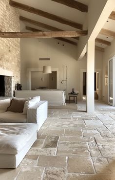 a living room with stone floors and exposed beams on the ceiling, along with two white couches