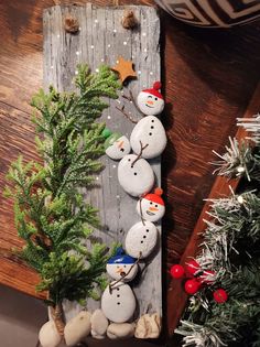 a wooden board with rocks and snowmen on it next to a christmas tree in the corner