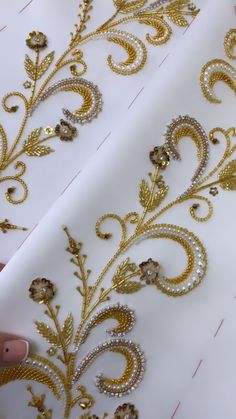 gold and white embroidered fabric being sewn on by hand, with scissors in the foreground