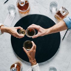 several people are holding their glasses in the middle of a table with drinks on it