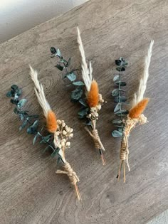 three dried flowers are sitting on a wooden table with green leaves and other things attached to the stems