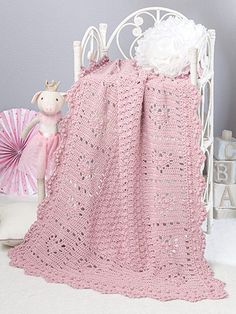 a pink crocheted blanket sitting on top of a bed next to a stuffed animal