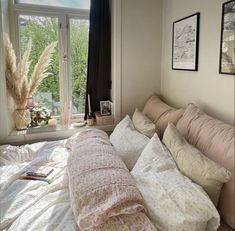 an unmade bed in front of a window with lots of pillows and blankets on it