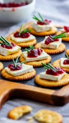 crackers with cranberry sauce and cheese on them are arranged on a wooden board