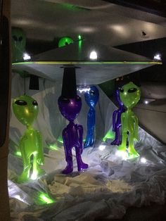 some alien statues are lit up in green and purple lights, while others look on