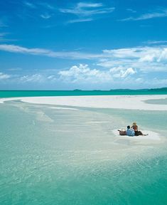 two people are sitting on a small boat in the middle of an empty beach with clear blue water