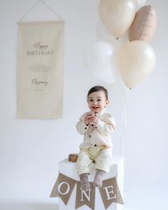 a baby sitting on top of a cake with balloons in the background and a happy birthday banner